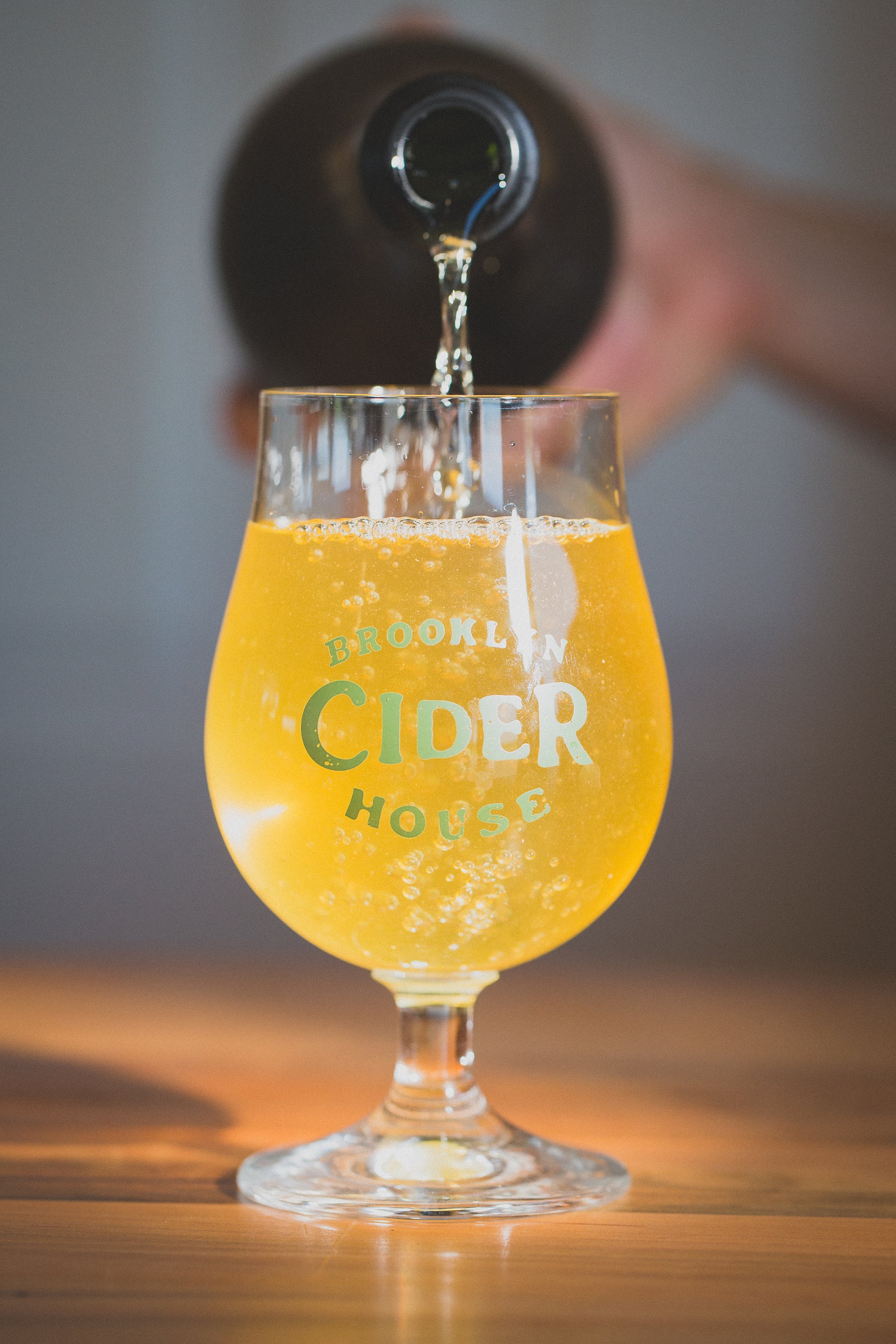 A close-up of a glass of cider being poured at Brooklyn Cider House — the txotx ritual, where cider streams from the kupela barrel into a tilted glass