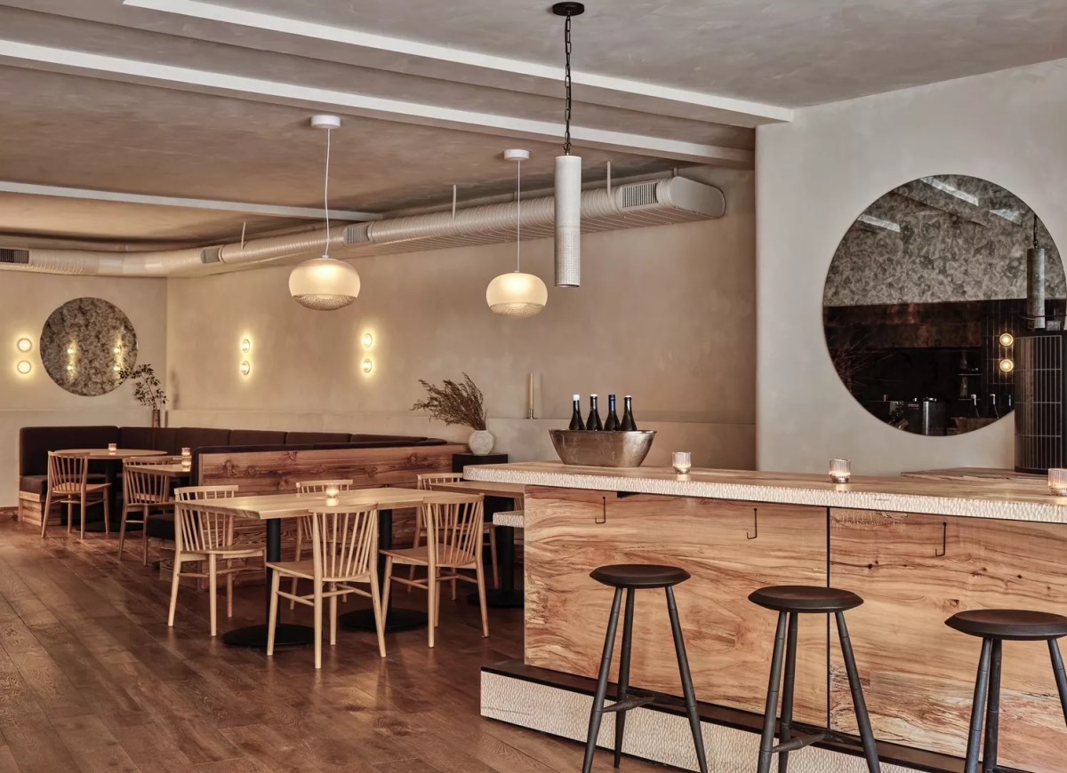 The Chleo dining room in daylight — terrazzo bar with spalted maple front, woven pendants, round mirrors, cream limewashed walls, light wood chairs and tables