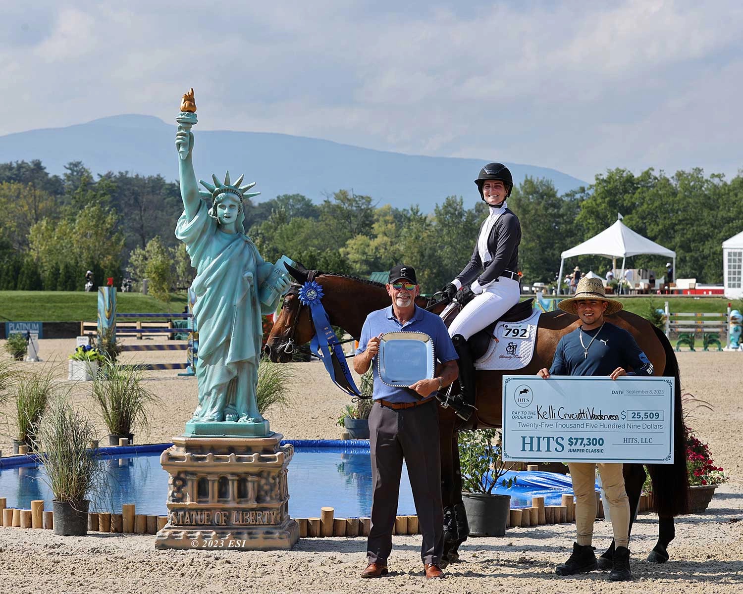 Kelli Cruciotti Vanderveen's winner ceremony at HITS on the Hudson — Statue of Liberty replica on the ring plinth, Catskill Mountains as backdrop