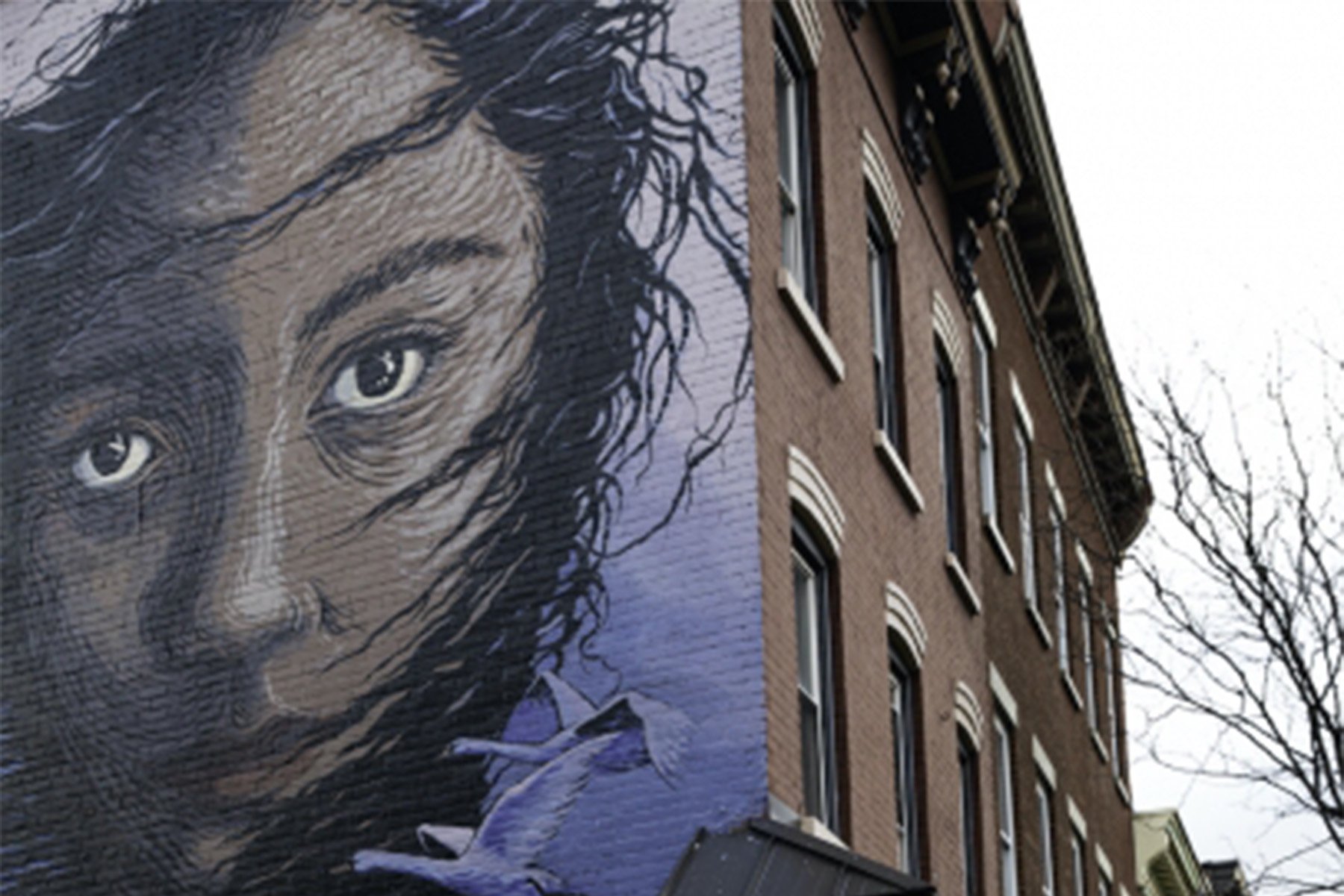 Six-story mural by Gaia in Midtown Kingston — Artemis Emerging from the Quarry, a portrait alluding to Kingston's stone and materials extraction history, against a brick building