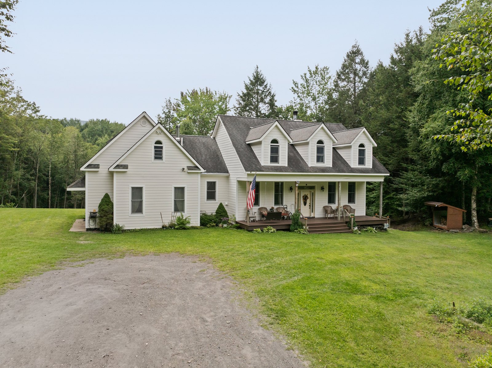 A white two-storey house with dormers seen from a gravel drive.