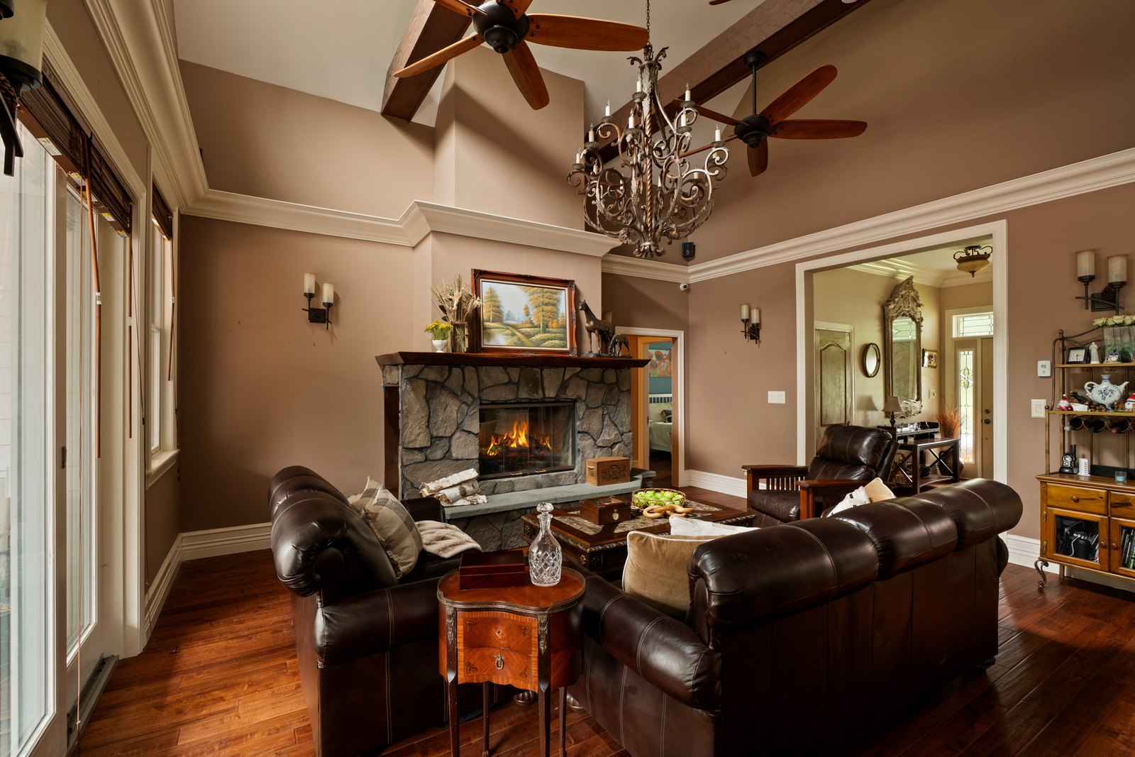 A stone fireplace lit in a beamed great room with leather seating.