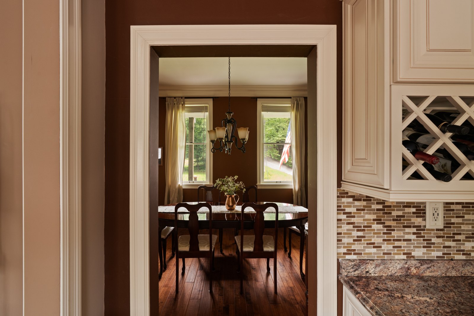 A dining room seen through a wide cased opening with a chandelier above the table.