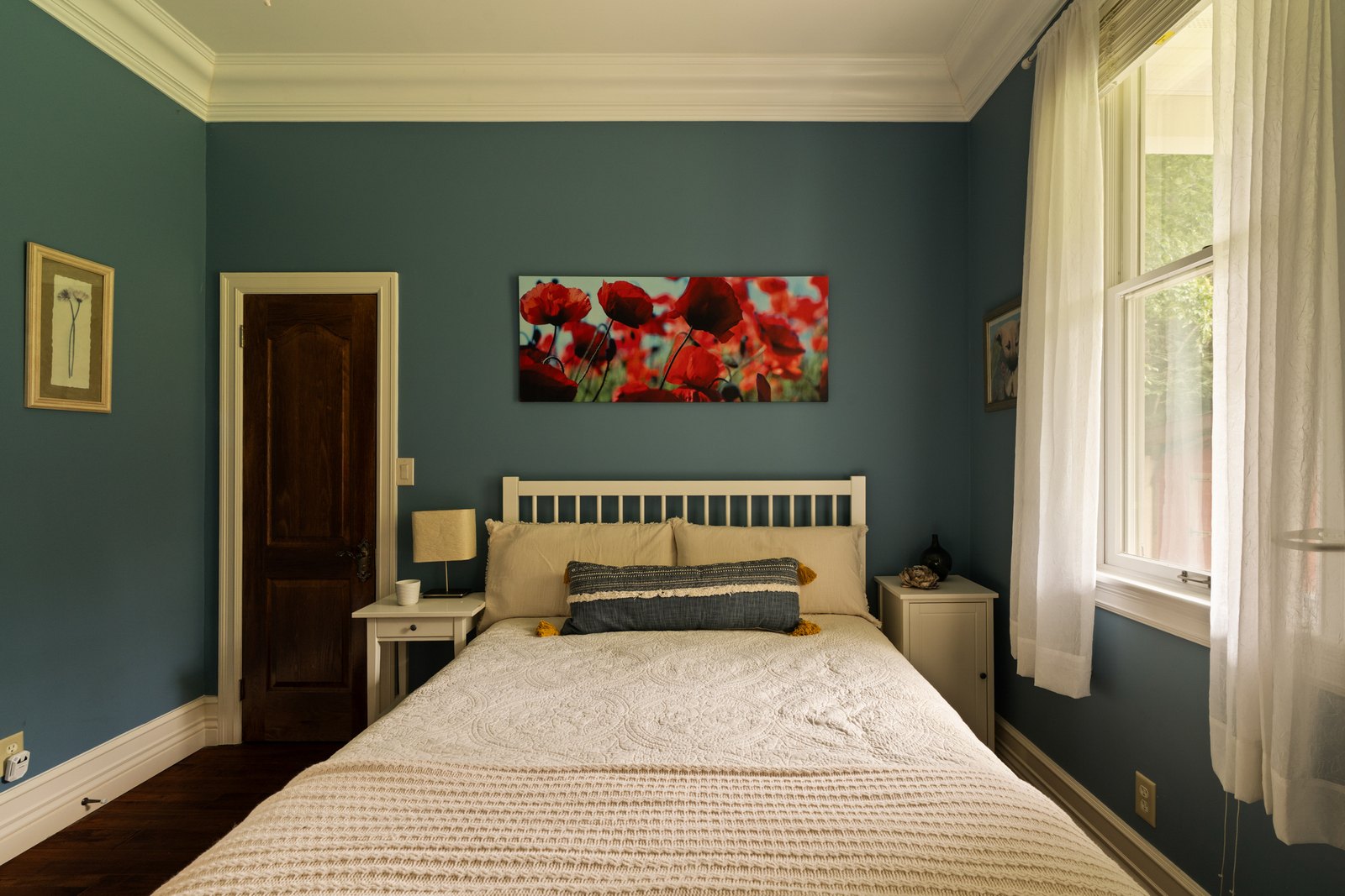 A bedroom with blue walls, a bed and tall curtained windows.