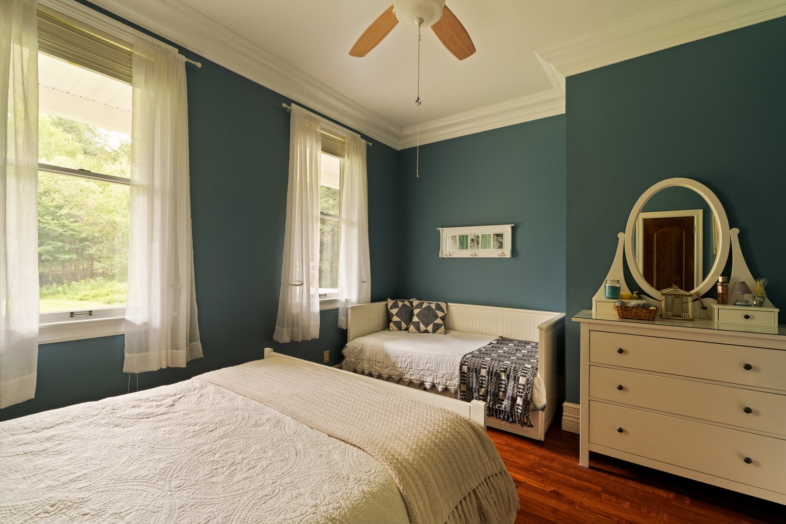 A bedroom with two beds, blue walls and a dresser with a mirror.