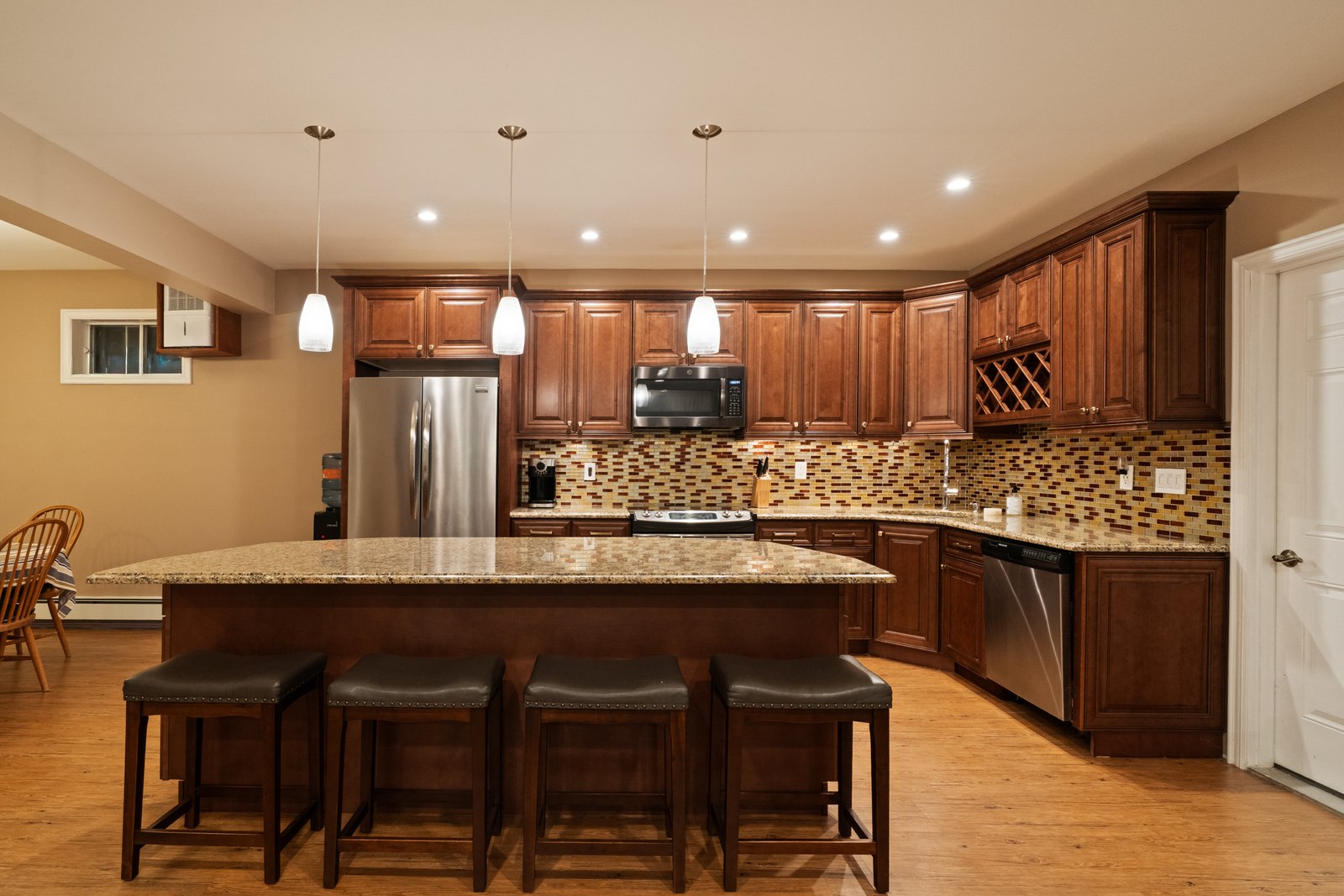 A kitchen with dark wood cabinetry, granite counters and an island with stools.