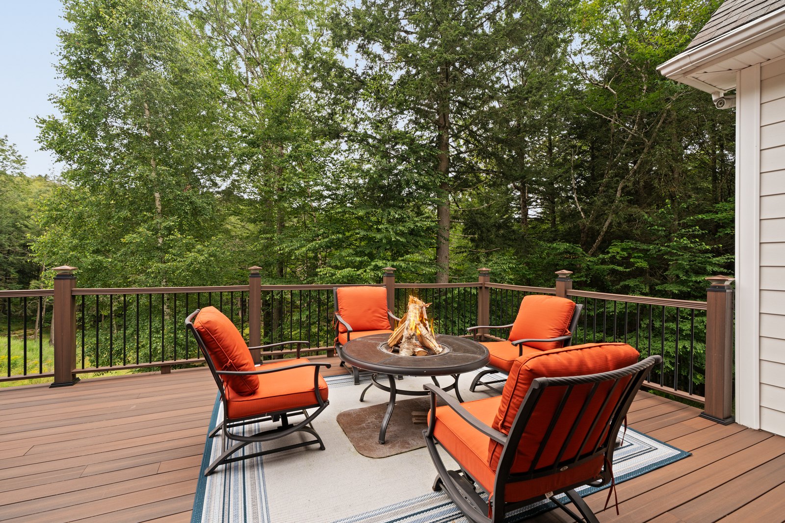 A deck with a fire pit and orange chairs surrounded by forest.