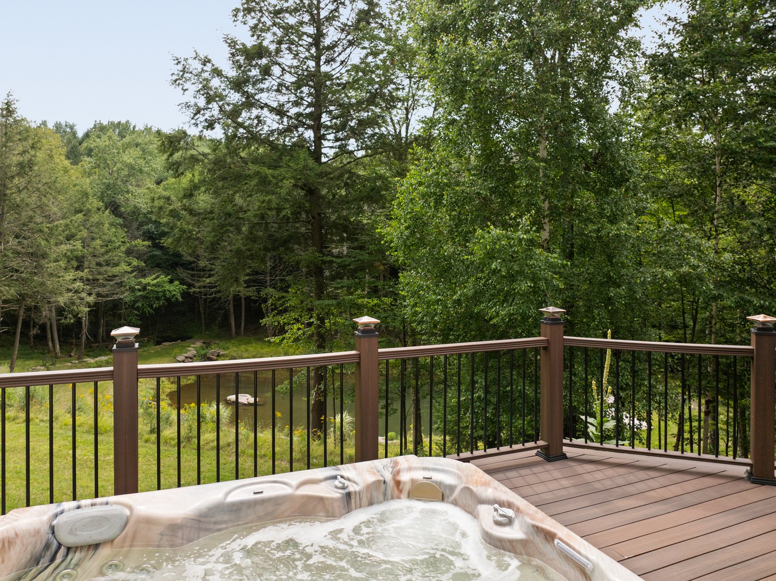 A hot tub on a deck with a railing and dense forest beyond.
