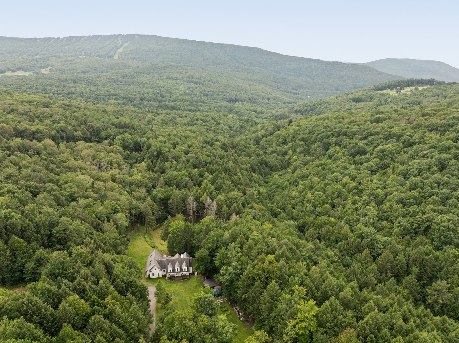Aerial view over forested Catskill ridgeline with a house among the trees.