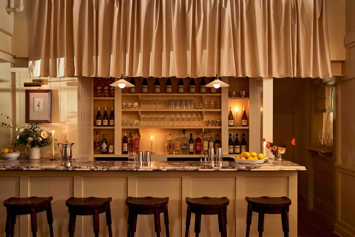 The bar at Little Goat — Calacatta Viola marble counter, brass pendants, candlelight, cream curtained shelving