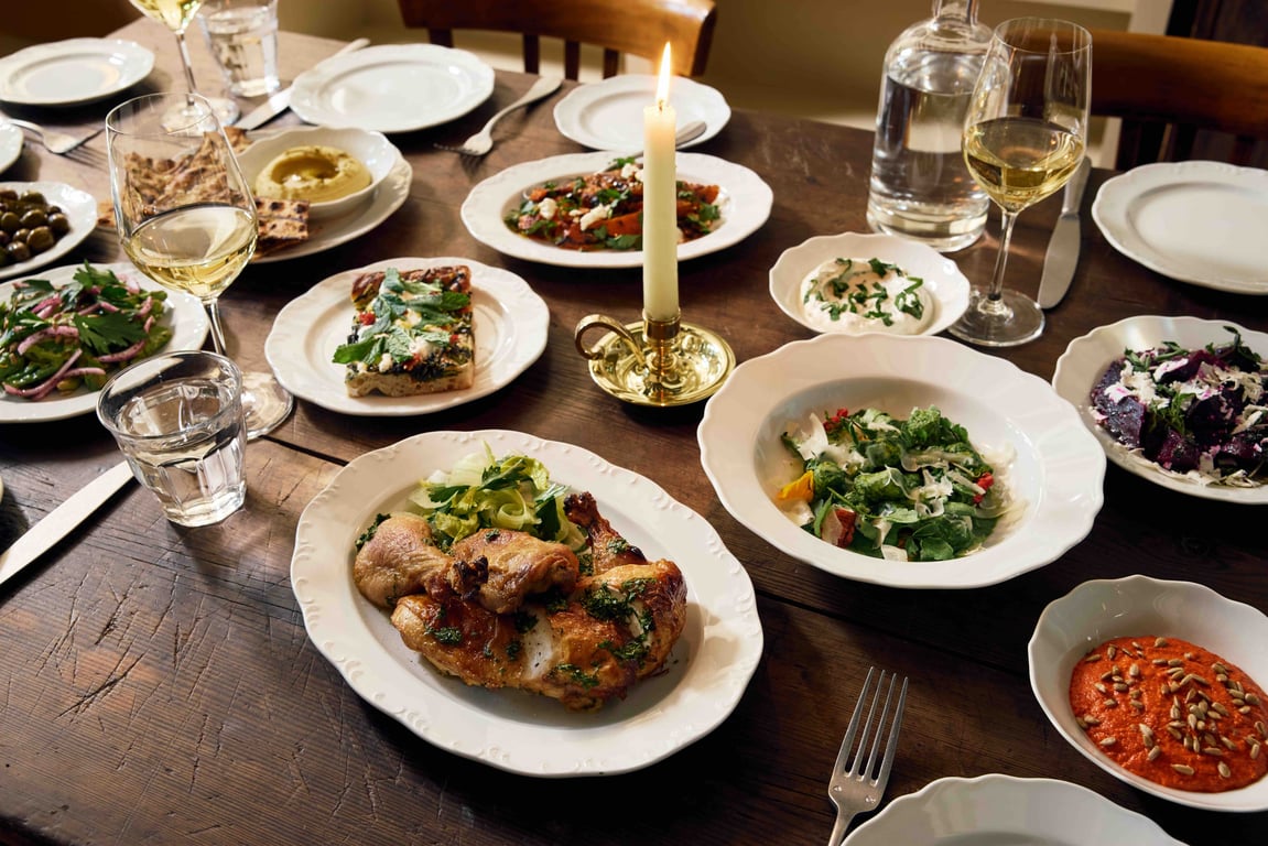 A dinner spread at Little Goat — roasted chicken, salads, hummus, candlelight on a wood farm table