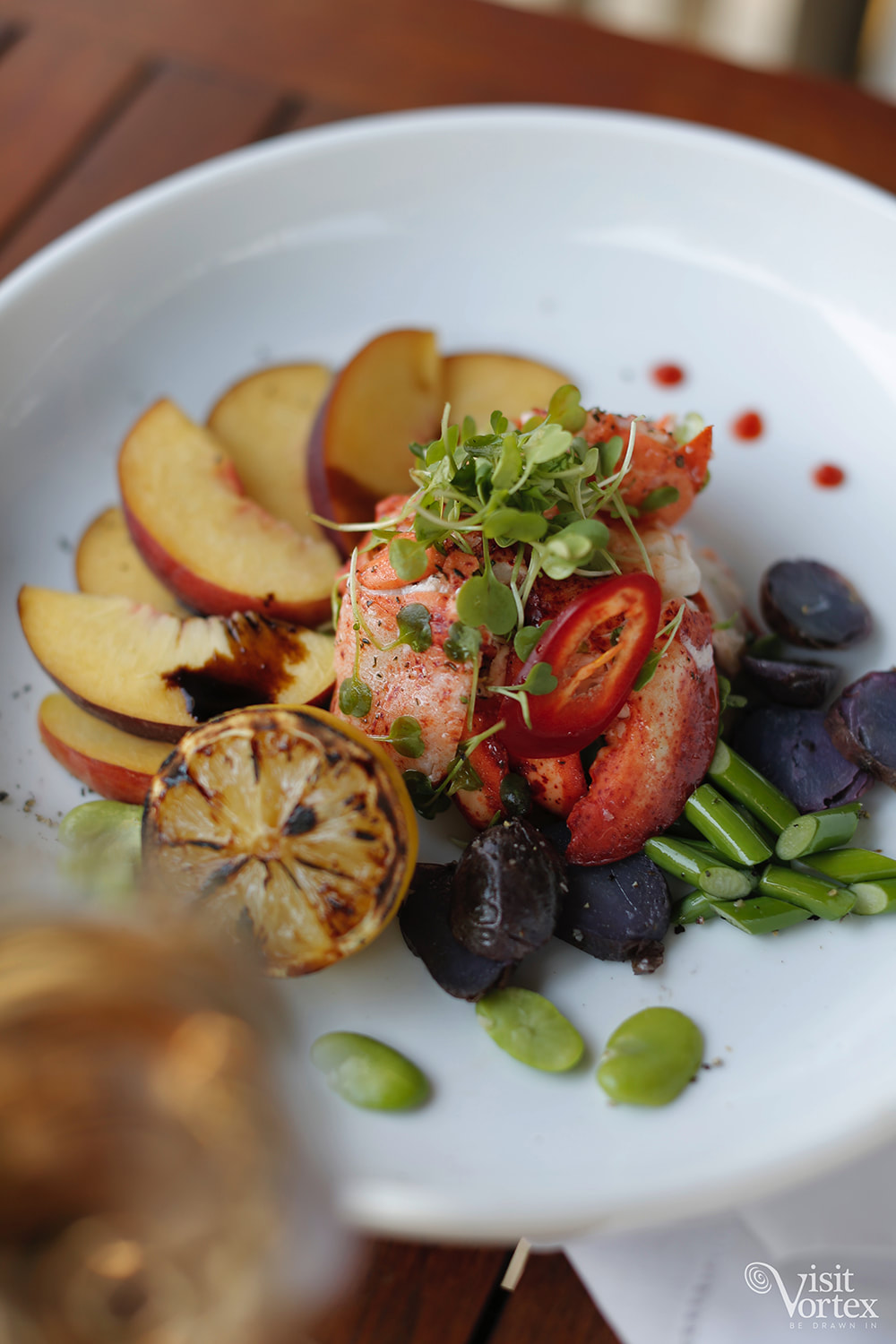 A restaurant-plated dish from Main Course — lobster tail with grilled peach, fingerling potatoes, microgreens, charred lemon on a white plate