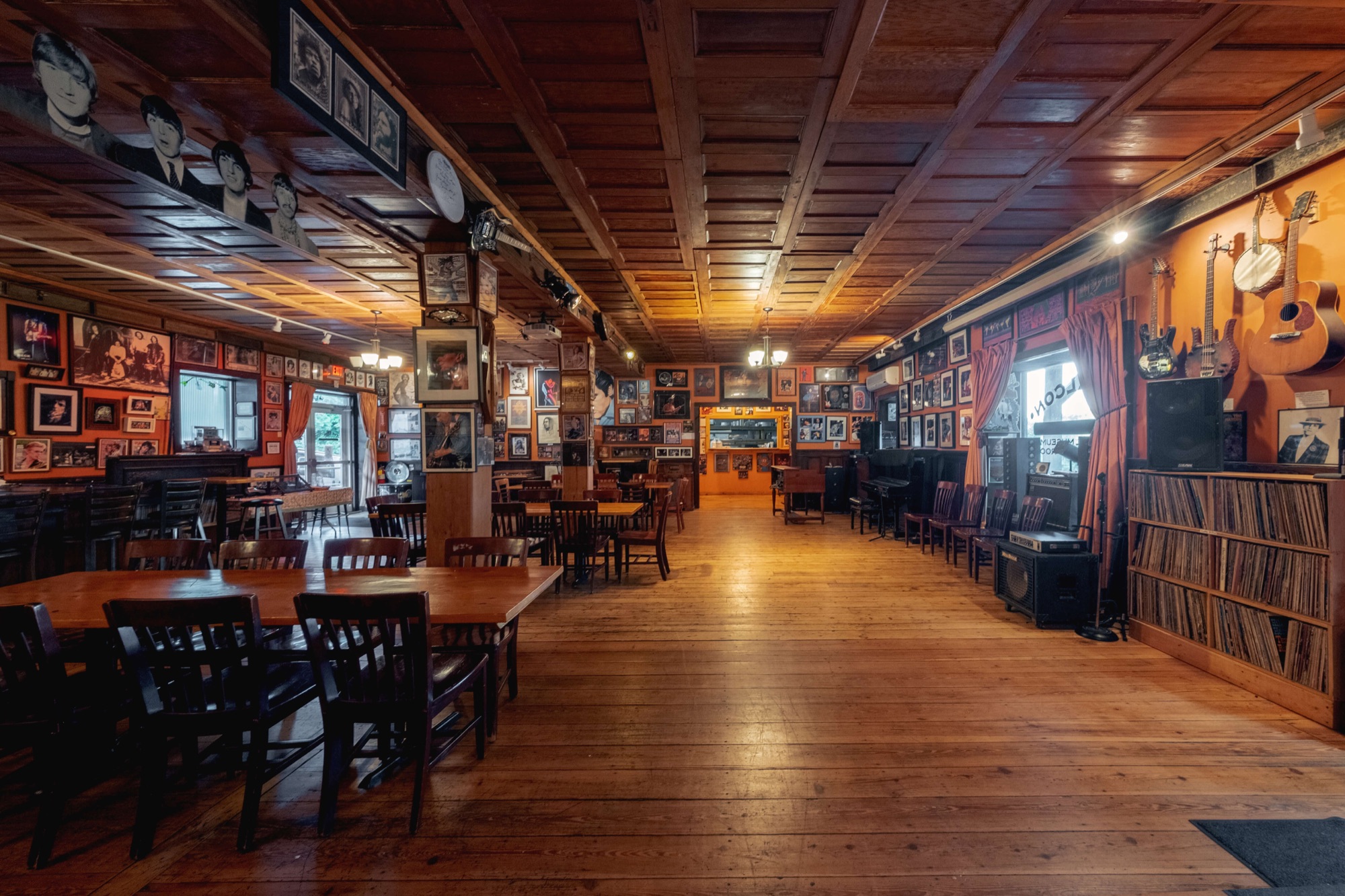 The Falcon's main performance room — wood-clad walls hung with framed musician portraits and album art, hardwood floor, café tables, an upright vinyl rack along the right wall