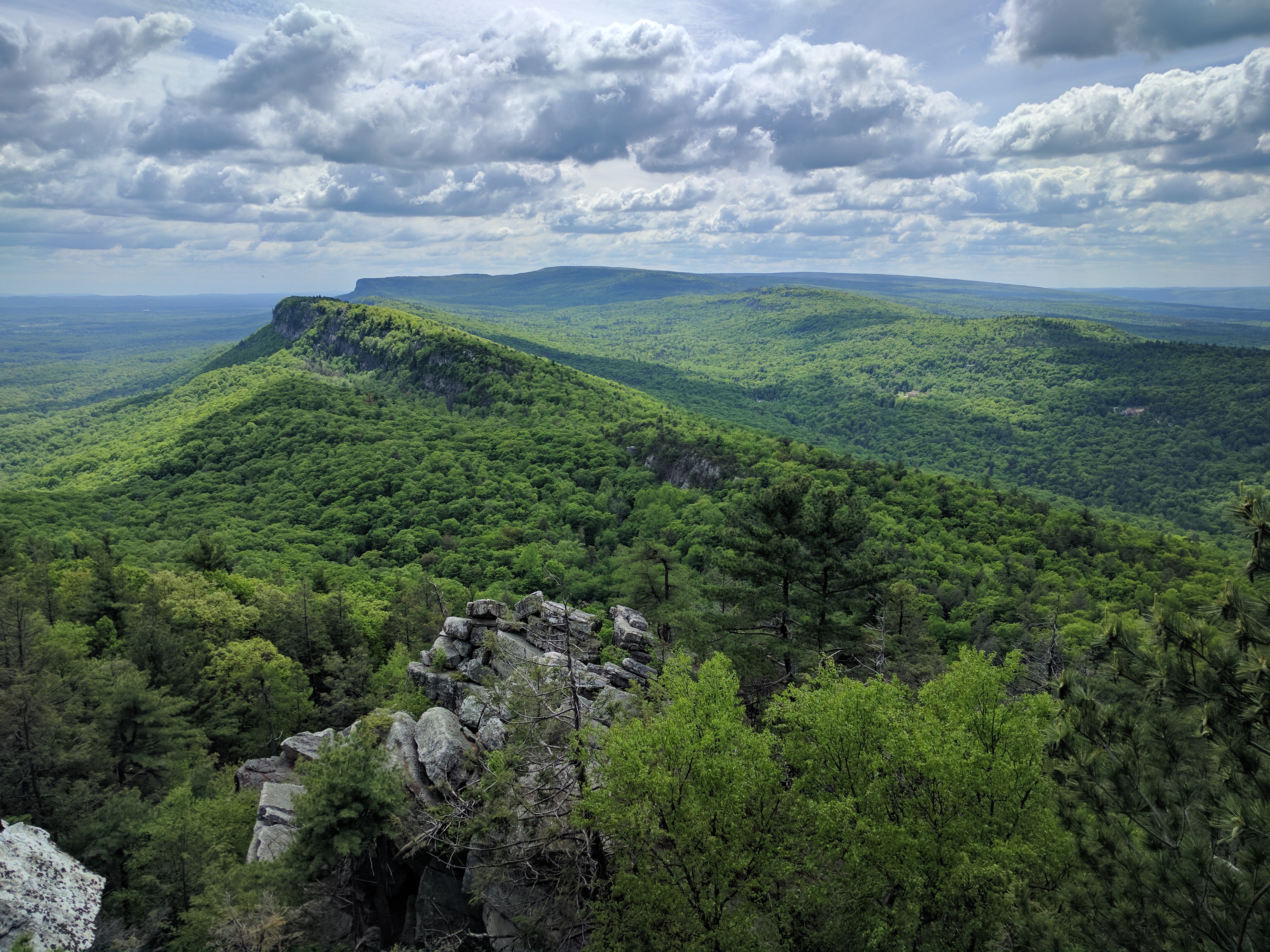 A view across the Shawangunk Ridge from a Mohonk Preserve hiking trail — layered blue mountains, autumn forest below, no development visible on the ridge
