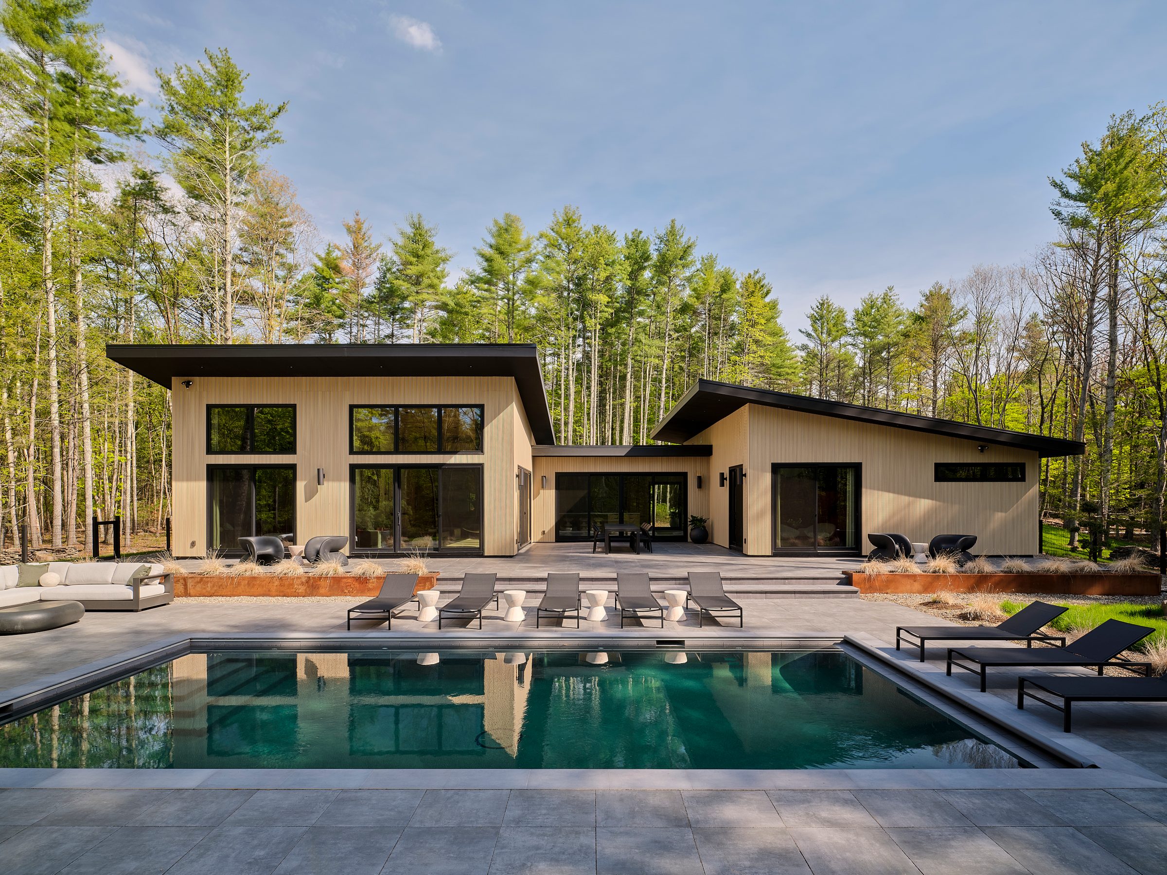 The pool and terrace in front of the house, with pines behind.