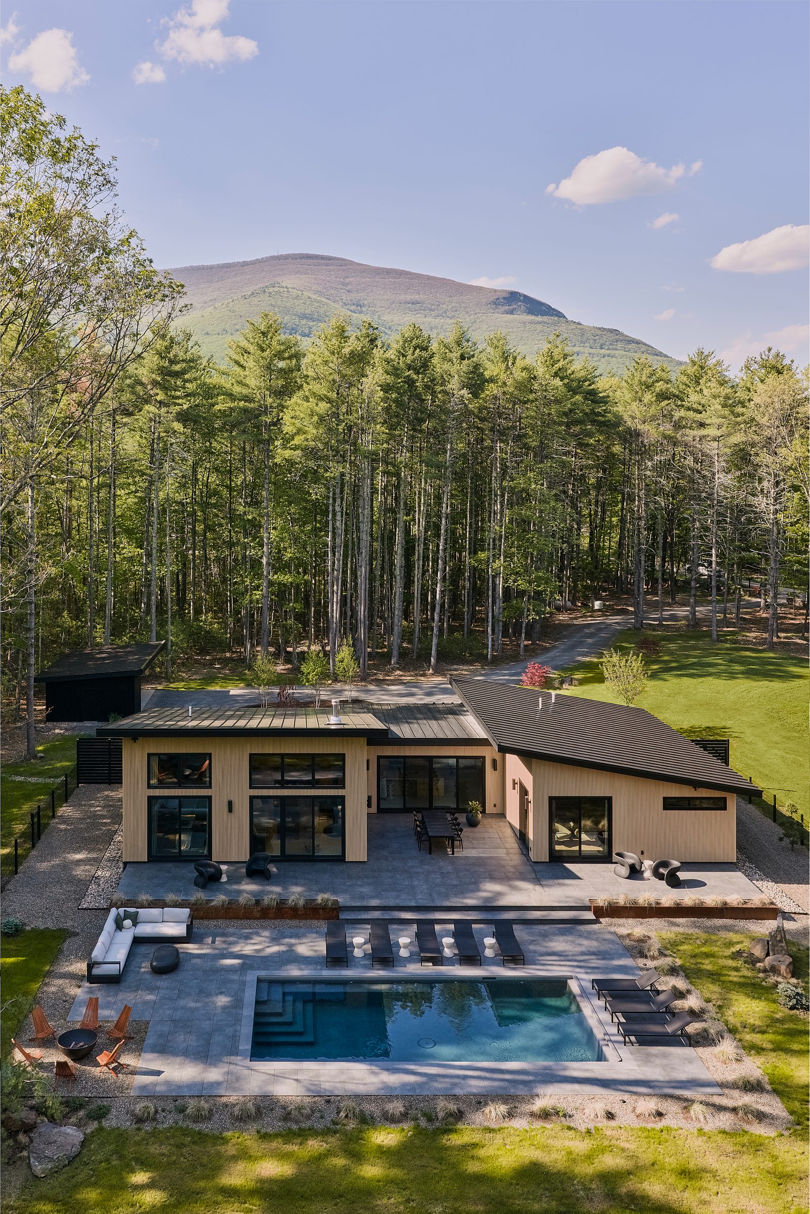 Aerial view of the house and pool in a clearing, a mountain beyond.