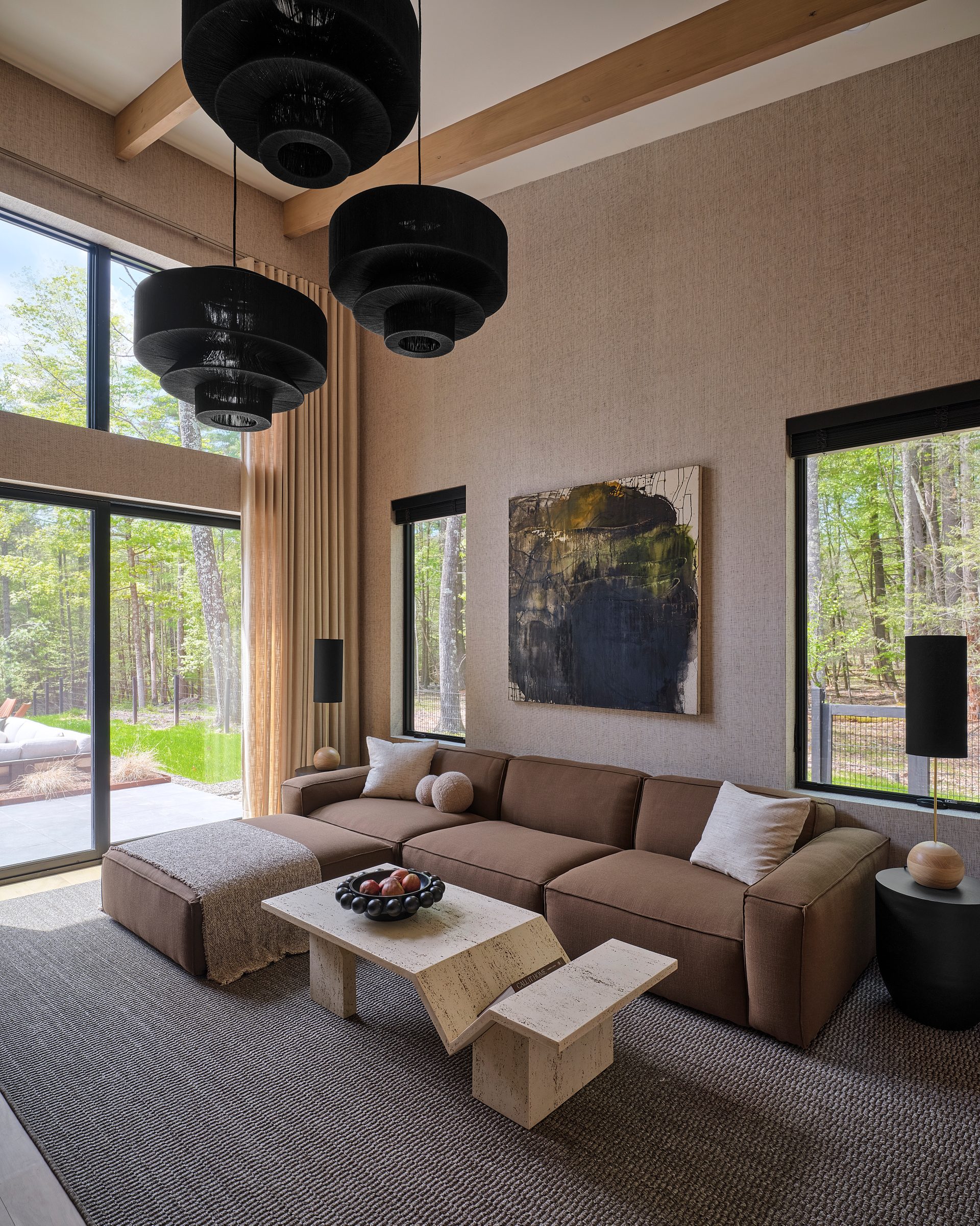 A living room with a sectional sofa, black pendant lights and tall windows.