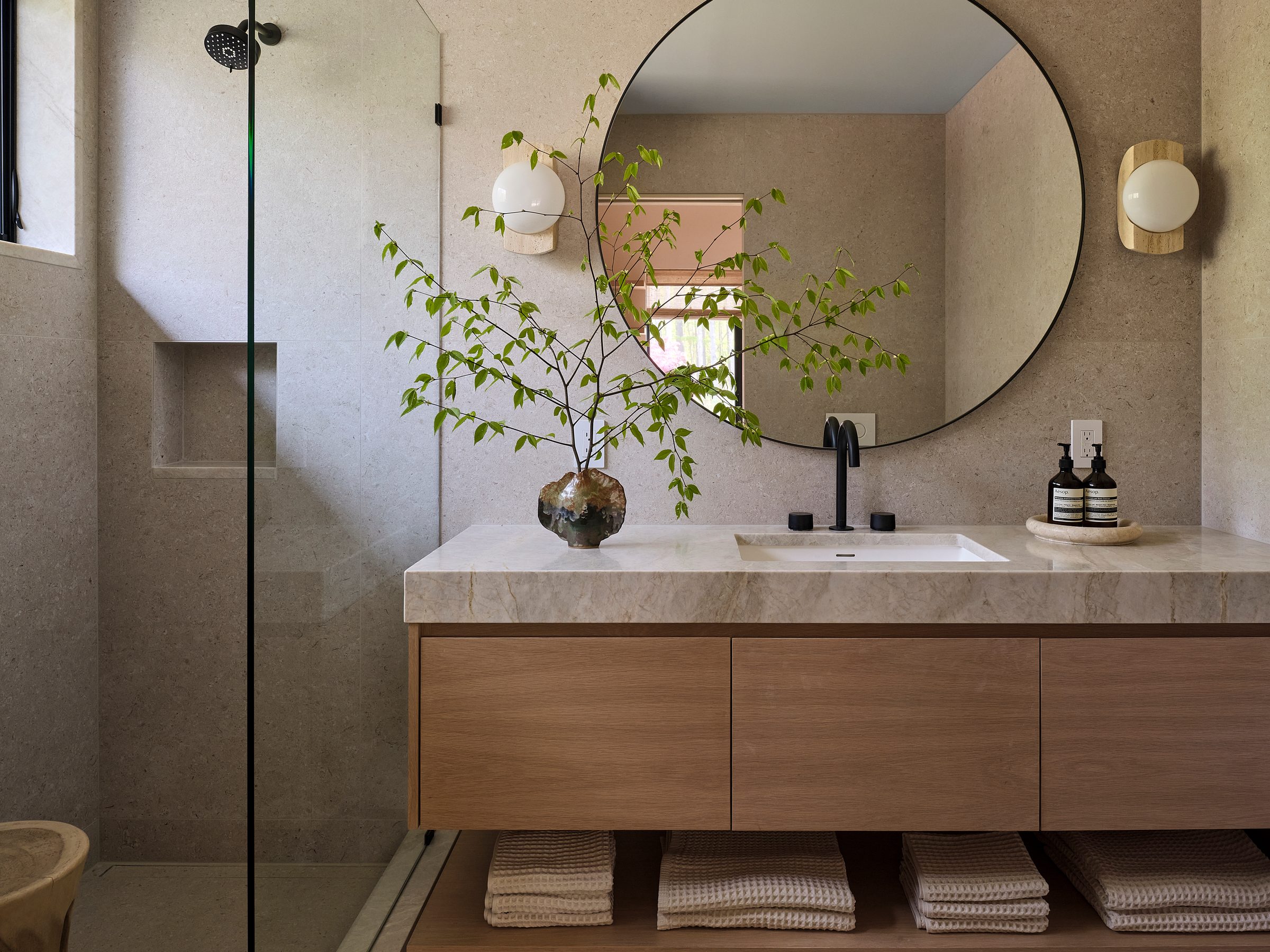 A bath with a glass shower, a round mirror and a floating stone vanity.