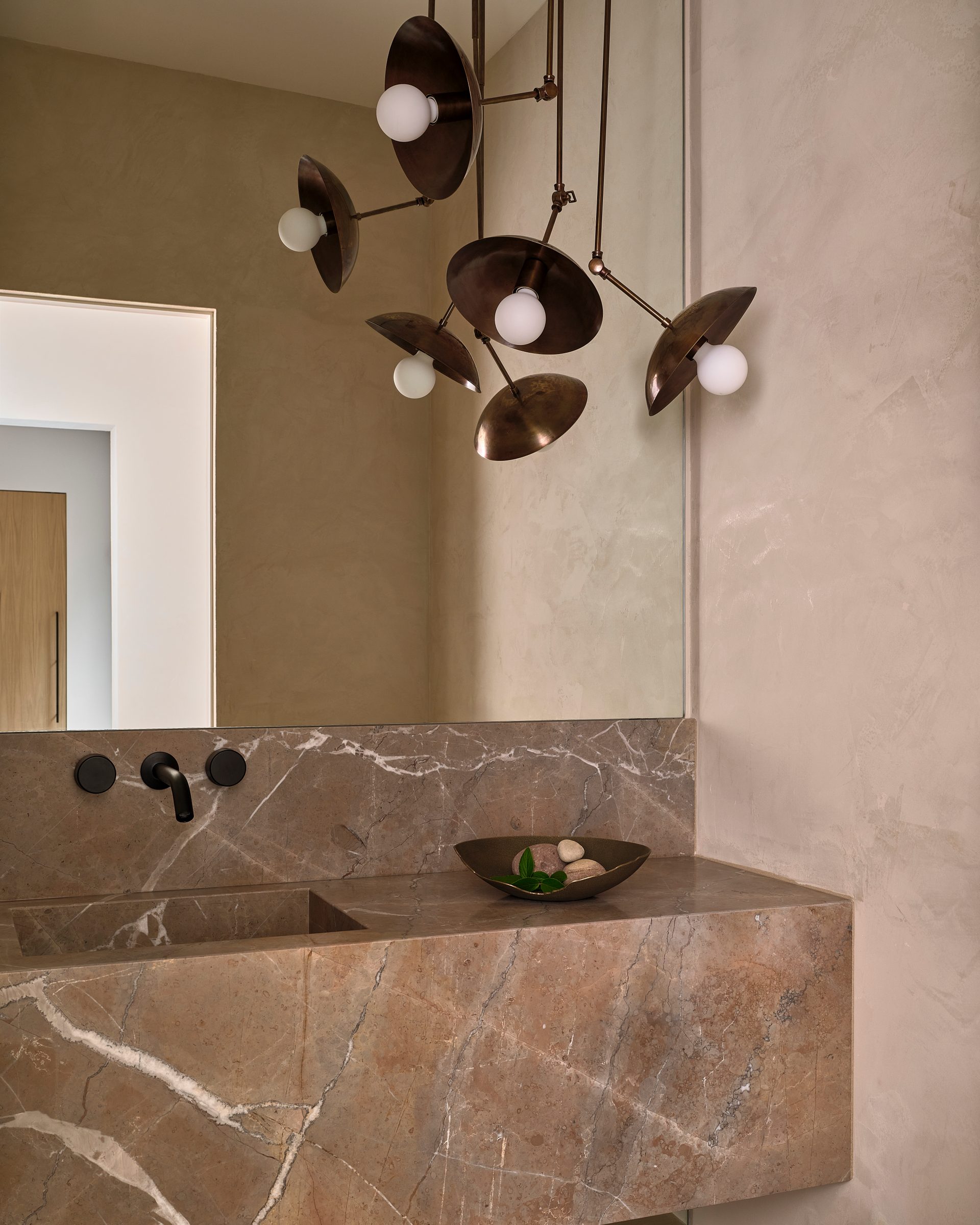 A powder room with a sculptural stone sink and a brass pendant.