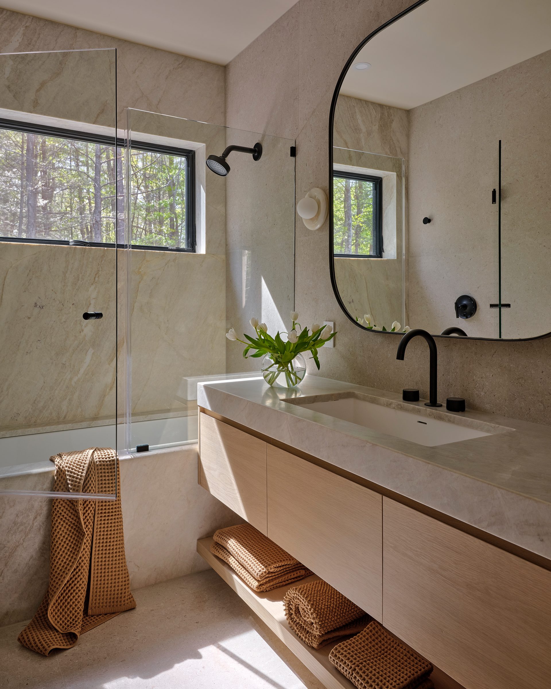 A bath with a stone vanity, an arched mirror and a shower.