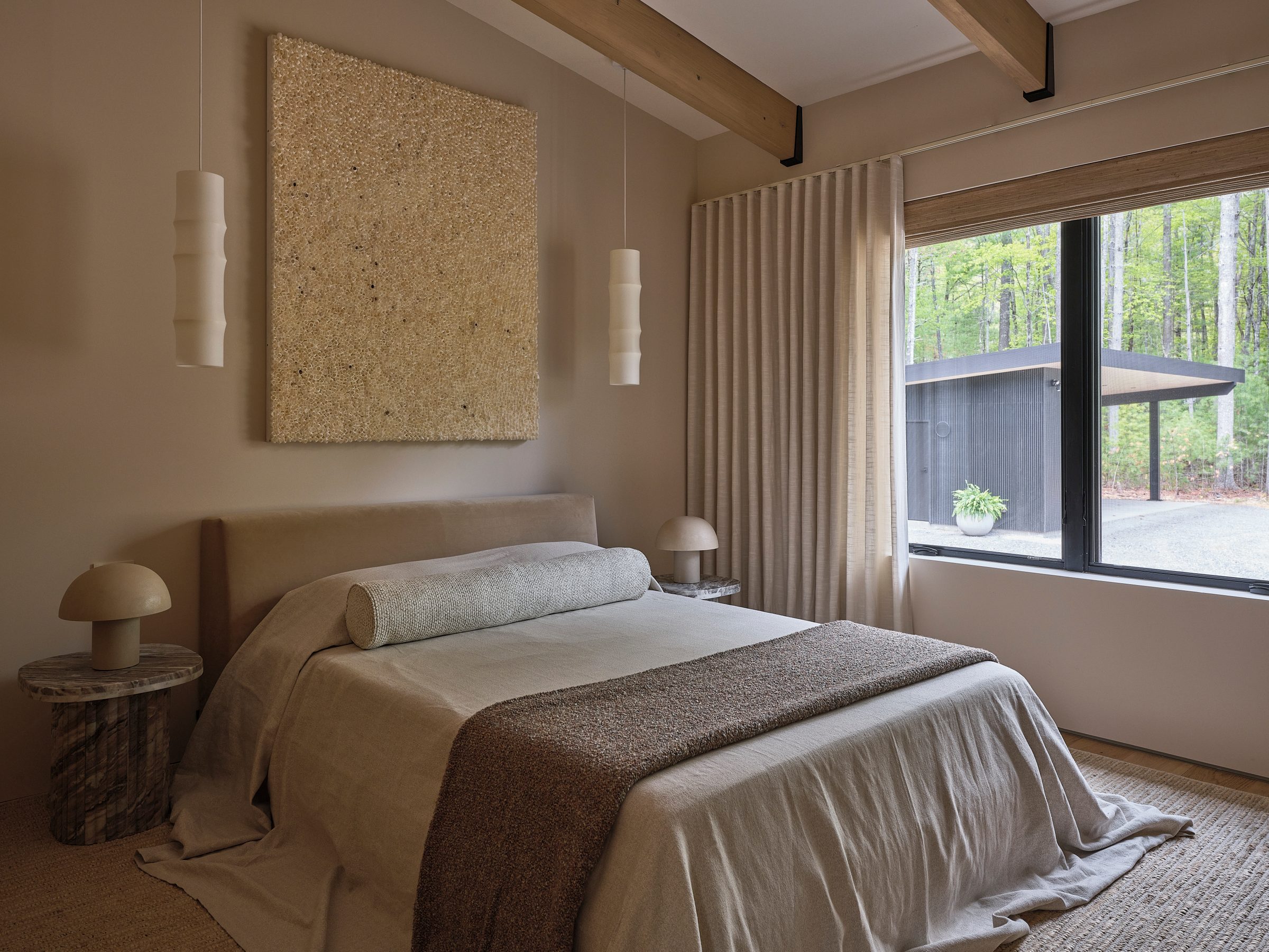 A bedroom with linen bedding, textured art and a window to the trees.