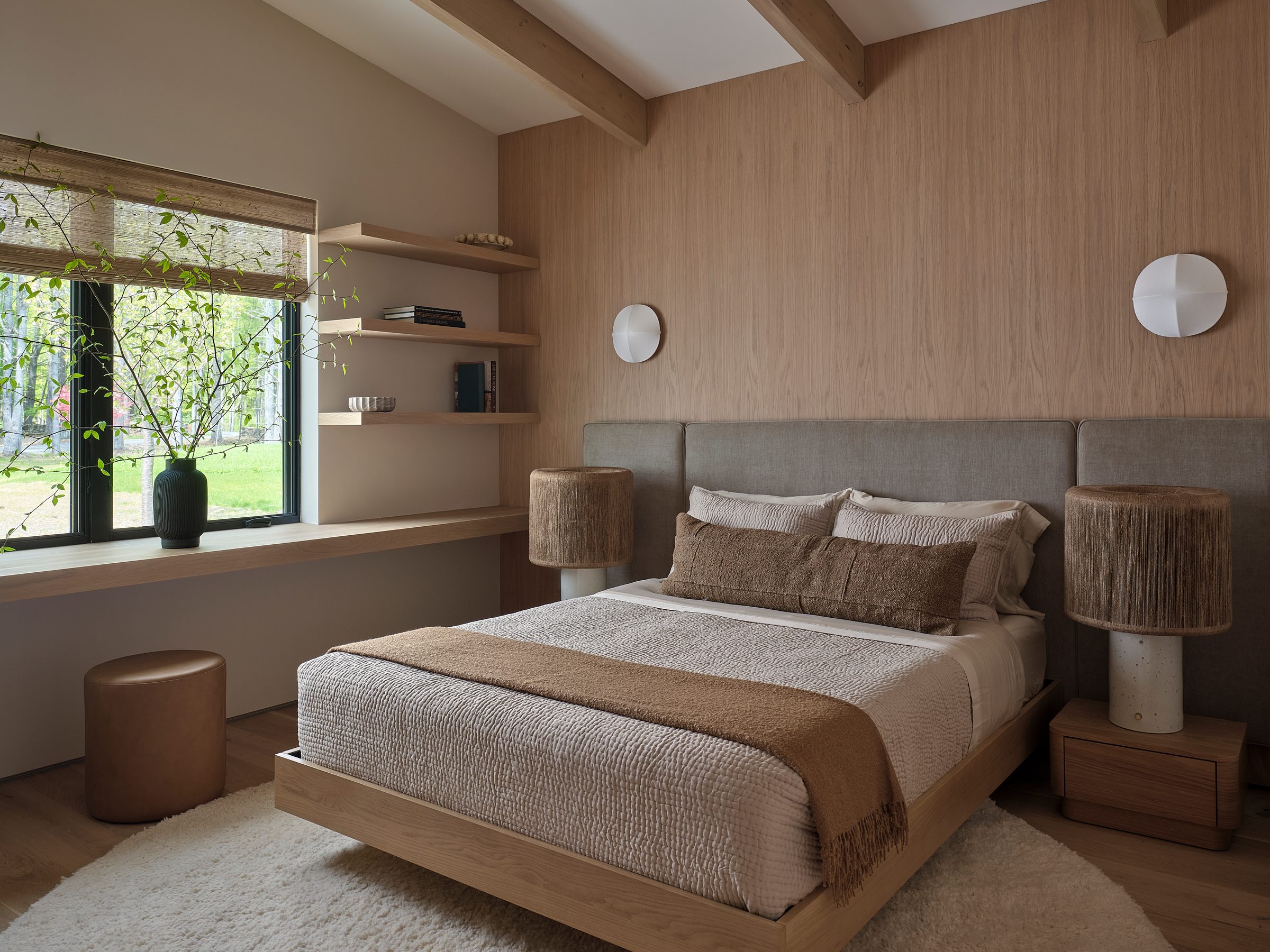 A bedroom with a wood-paneled wall, a built-in shelf and a window.