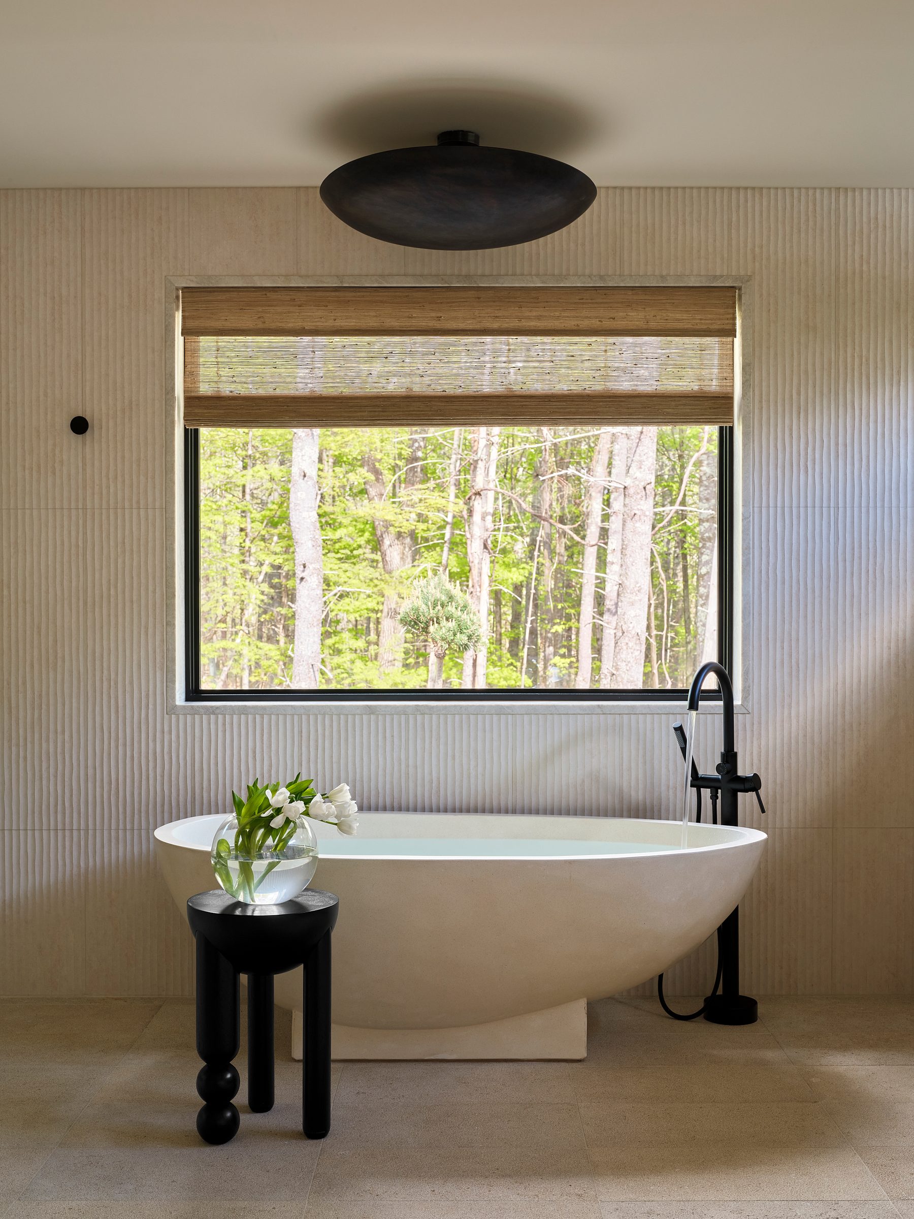A terrazzo soaking tub on limestone, beneath a window to the woods.