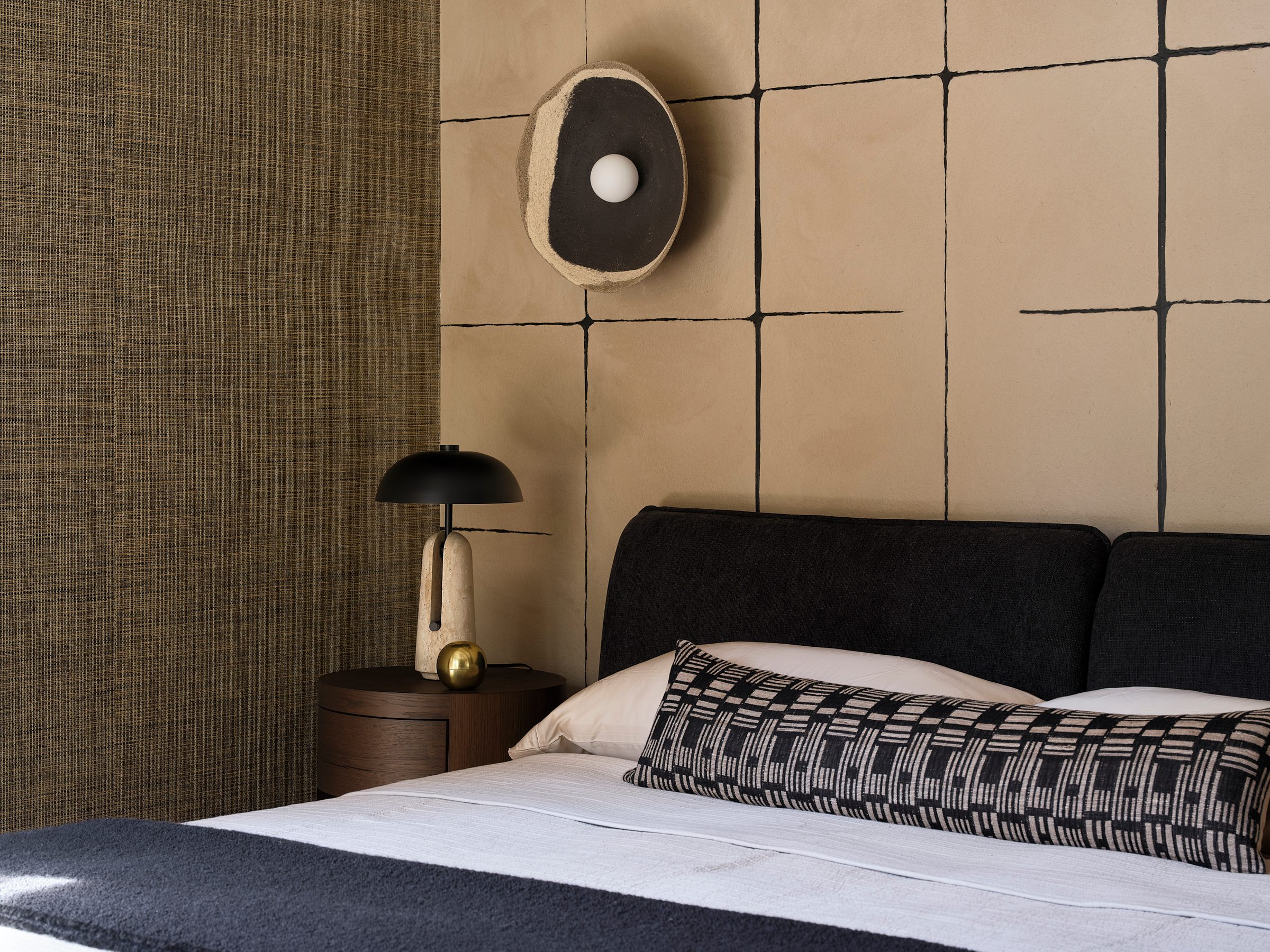 A bed with a dark upholstered headboard and sculptural wall lights.