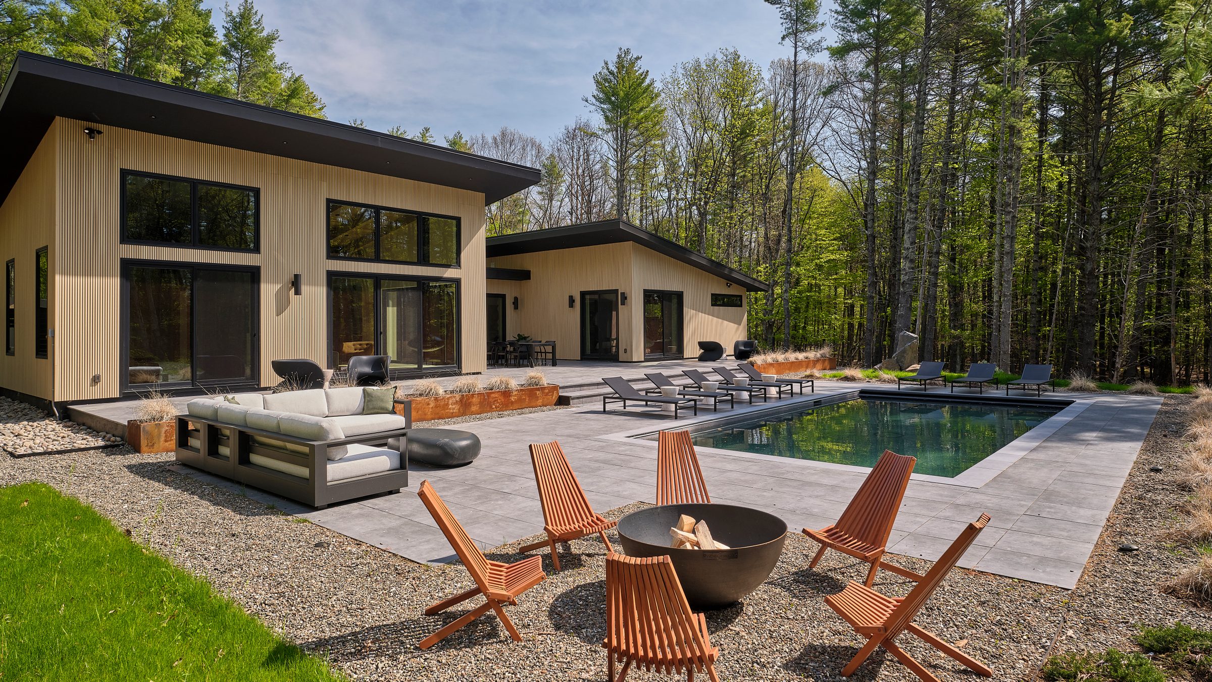 A wood-burning fire pit with wooden chairs beside the pool terrace.