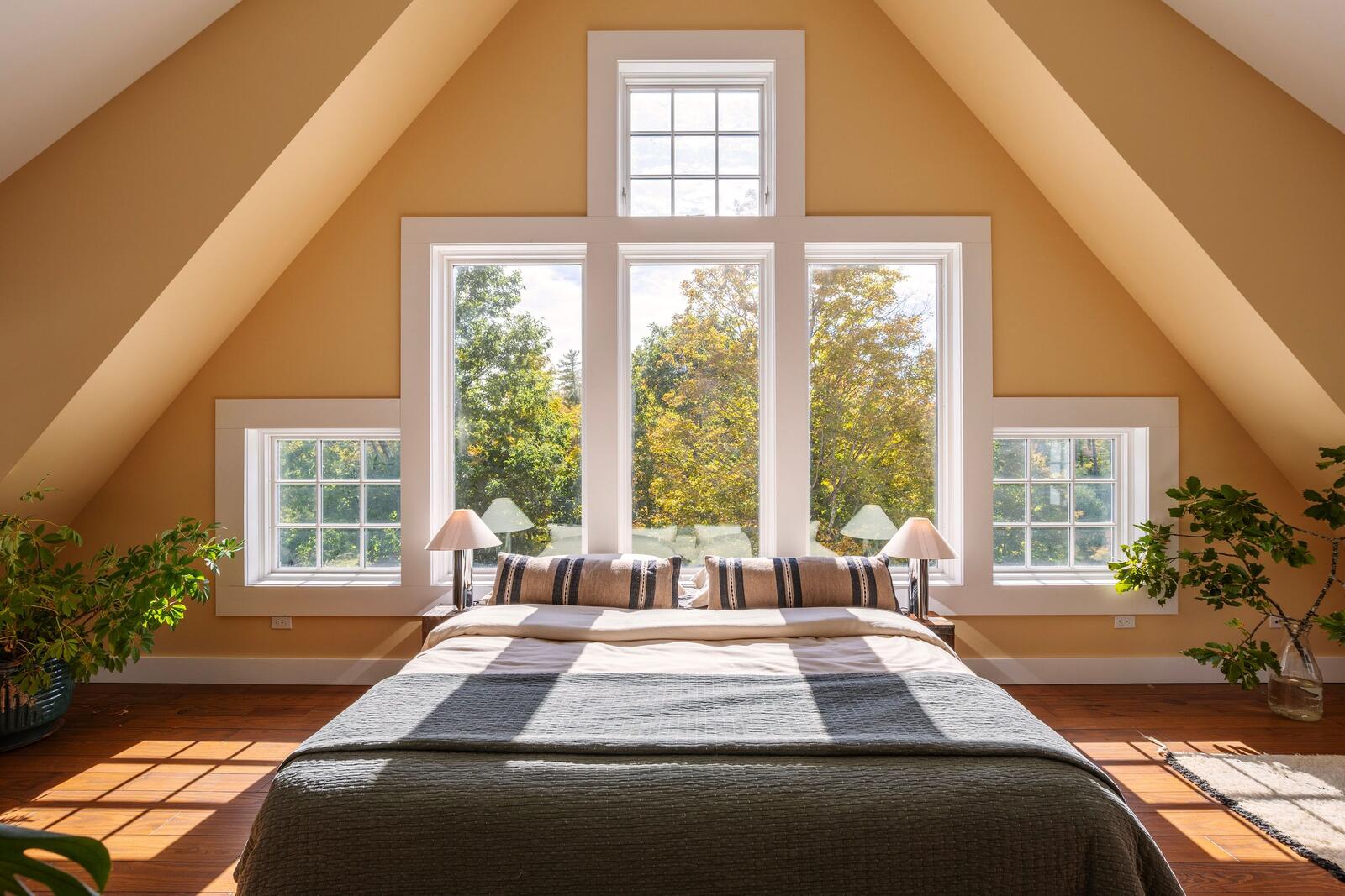 A bedroom under the eaves, a tall window at its center.