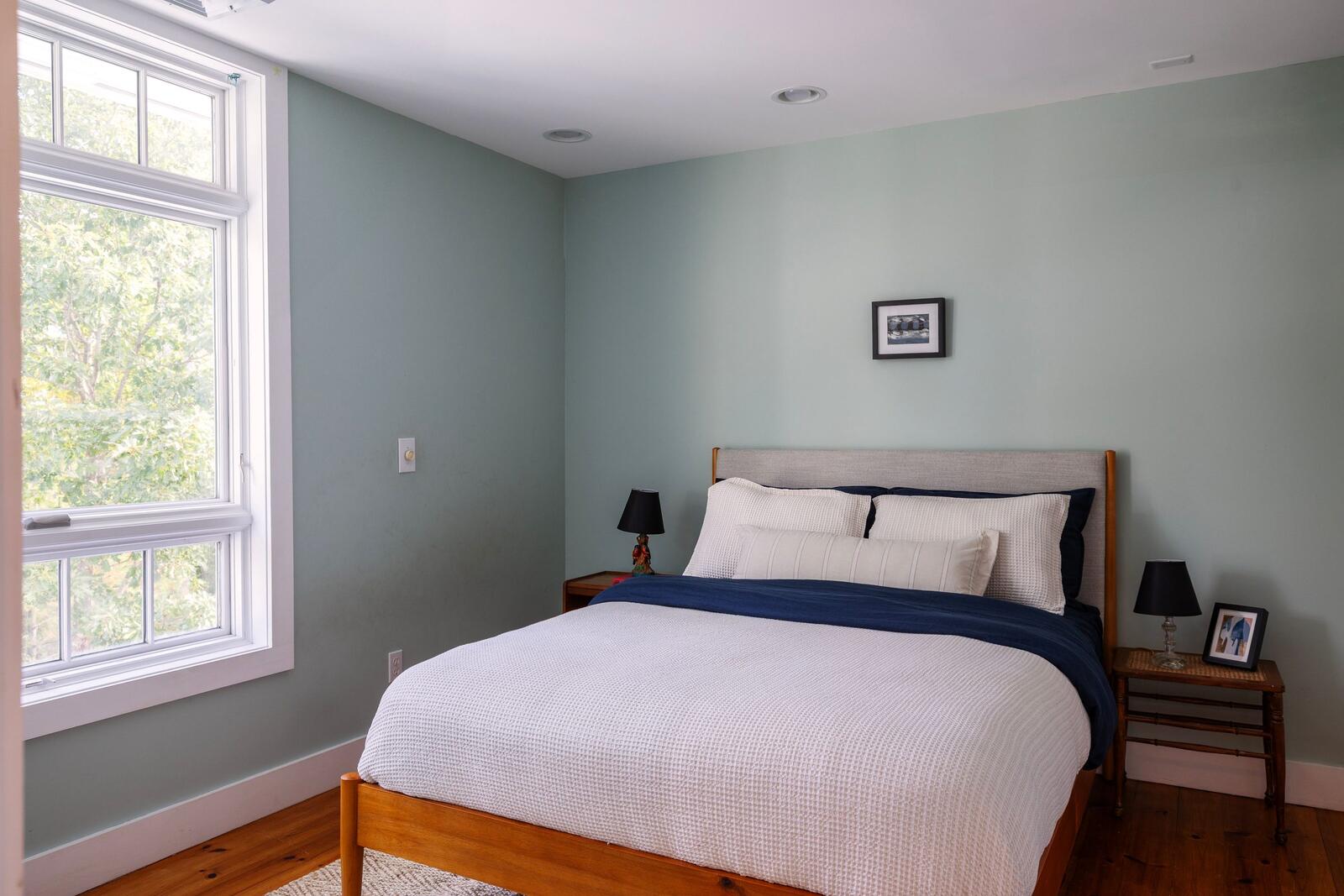 A bedroom in soft blue, two windows to the trees.