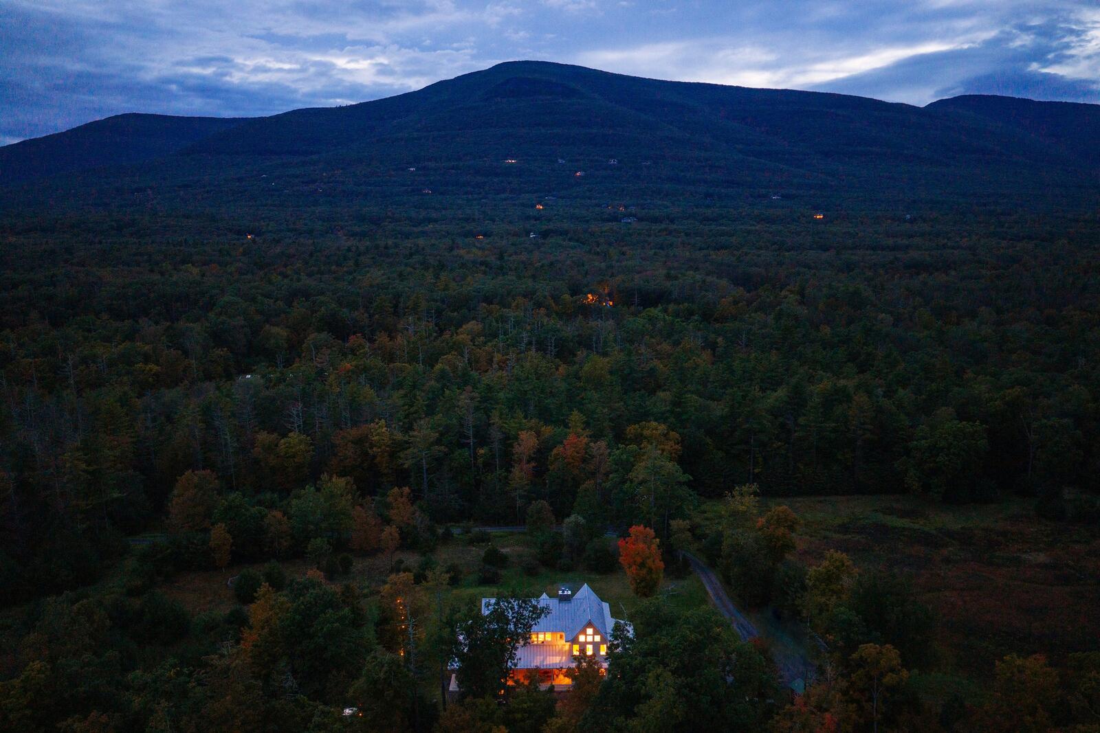 The house lit at dusk beneath the mountain.