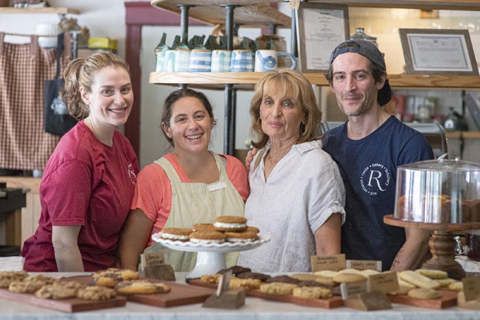 The Sasso siblings at Rosie General — Nicole, Andrea, Ashley, and Anthony behind the bakery counter, with the day's cookies on a marble cake stand